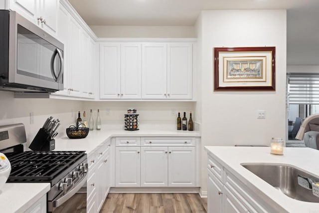 kitchen featuring a sink, light countertops, light wood-style floors, stainless steel appliances, and white cabinetry