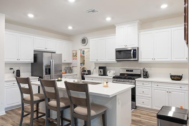 kitchen with an island with sink, stainless steel appliances, white cabinetry, and visible vents
