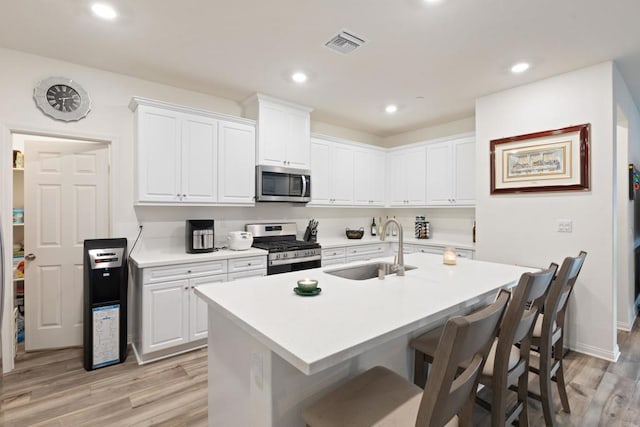 kitchen with visible vents, a breakfast bar area, a sink, light wood finished floors, and appliances with stainless steel finishes