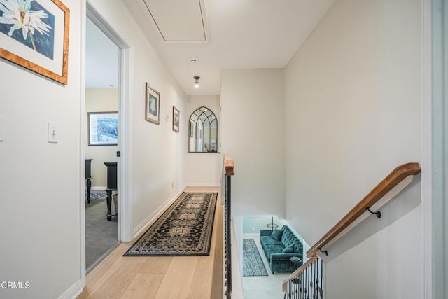 hall with attic access, wood finished floors, baseboards, and an upstairs landing