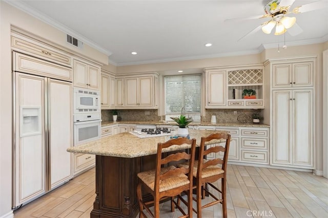 kitchen with built in appliances, cream cabinetry, decorative backsplash, and visible vents