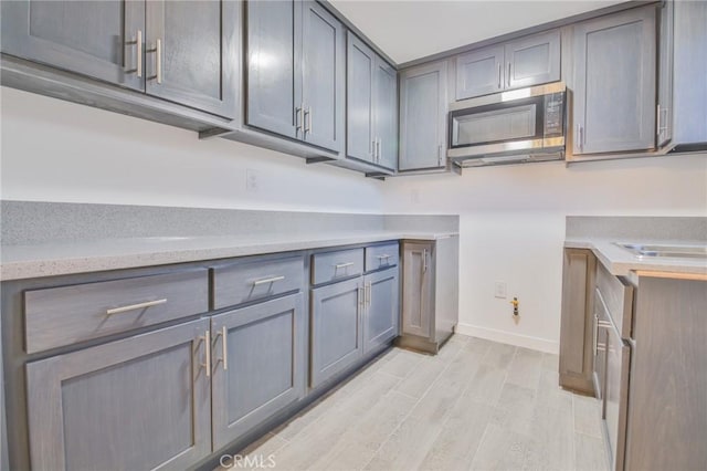 kitchen featuring light countertops, baseboards, stainless steel microwave, light wood-style floors, and gray cabinets