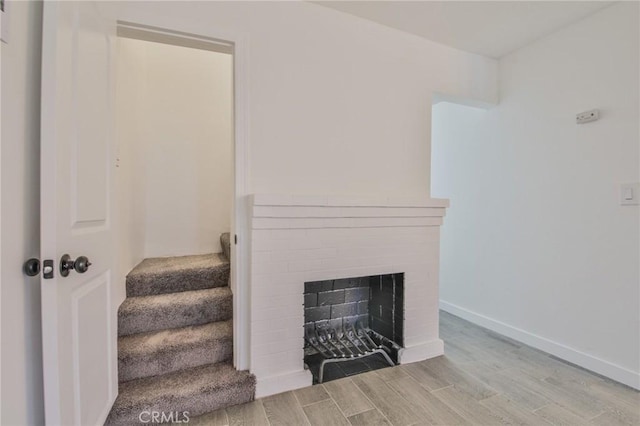 staircase featuring a brick fireplace, baseboards, and wood finished floors