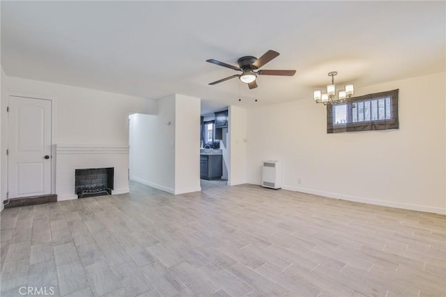 unfurnished living room featuring baseboards, a fireplace, ceiling fan with notable chandelier, and light wood finished floors