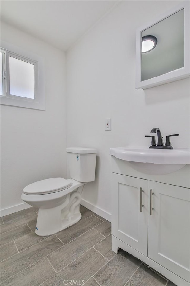 half bathroom with baseboards, toilet, vanity, and wood finish floors