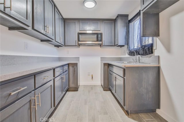kitchen with light countertops, stainless steel microwave, baseboards, a sink, and light wood finished floors
