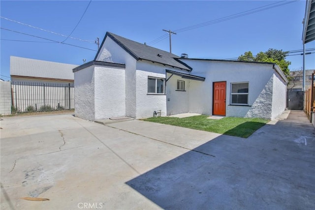 rear view of house featuring stucco siding, fence, a lawn, and a patio area