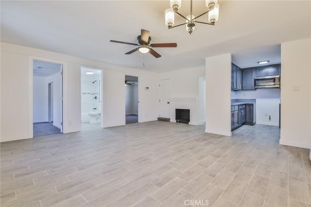 unfurnished living room featuring ceiling fan with notable chandelier, a fireplace, light wood-style floors, and baseboards