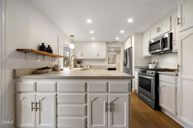 kitchen featuring a sink, appliances with stainless steel finishes, a peninsula, white cabinetry, and wood finished floors