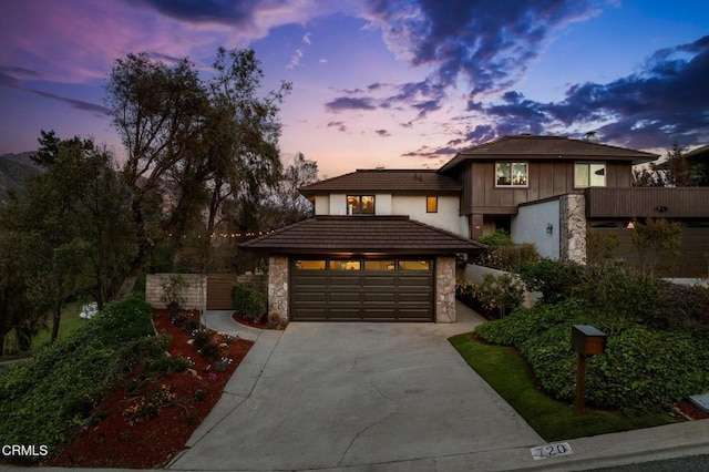 prairie-style home with a tiled roof, stone siding, a garage, and driveway