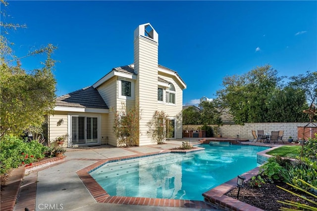 back of property featuring fence, a chimney, a patio area, and a fenced in pool