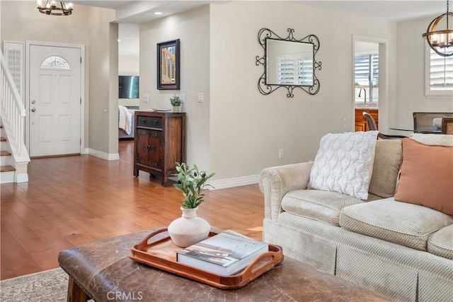 living area featuring baseboards, stairway, wood finished floors, and an inviting chandelier