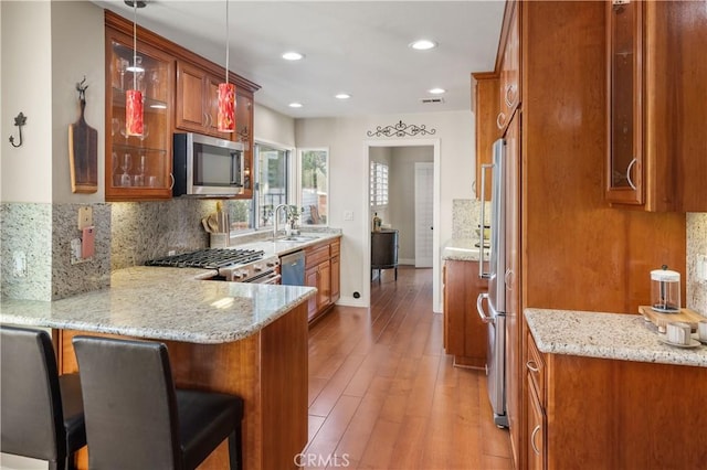 kitchen featuring stainless steel appliances, light stone countertops, recessed lighting, a peninsula, and brown cabinetry