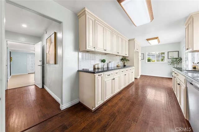 kitchen with cream cabinets, dark countertops, stainless steel dishwasher, and dark wood-style flooring