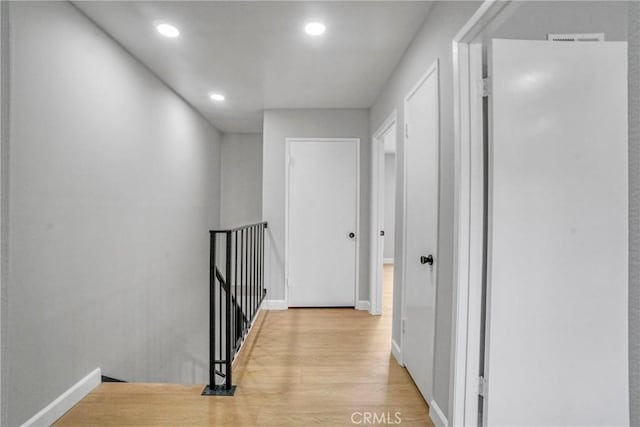 hallway featuring light wood-style floors, recessed lighting, baseboards, and an upstairs landing