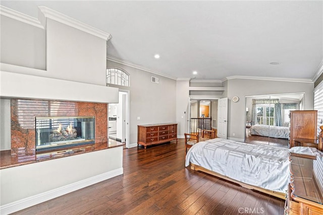 bedroom featuring a multi sided fireplace, hardwood / wood-style flooring, baseboards, ornamental molding, and recessed lighting