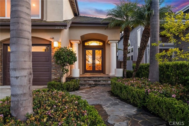 exterior entry at dusk with a garage, french doors, and stucco siding