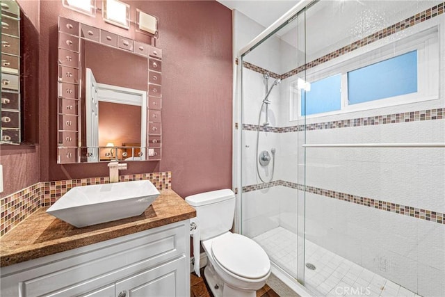 full bathroom featuring toilet, decorative backsplash, a shower stall, a textured wall, and vanity