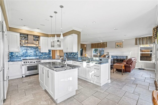 kitchen featuring high end stainless steel range, wall chimney exhaust hood, a peninsula, a sink, and a premium fireplace