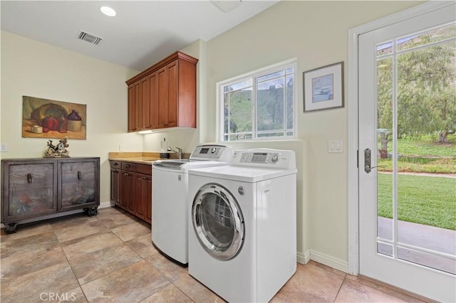 washroom featuring a wealth of natural light, visible vents, a sink, cabinet space, and washer and clothes dryer