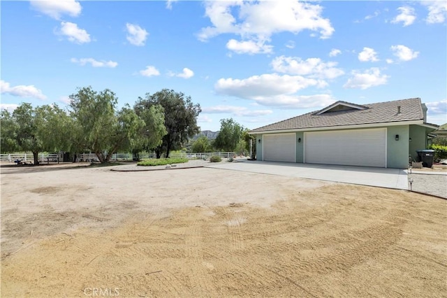 view of side of home featuring concrete driveway, stucco siding, and fence