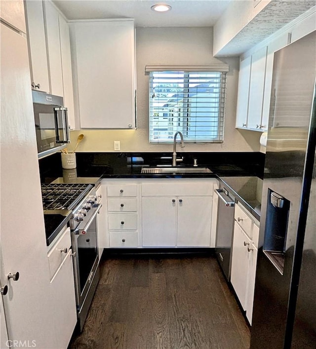 kitchen featuring a sink, appliances with stainless steel finishes, dark countertops, and dark wood-style floors