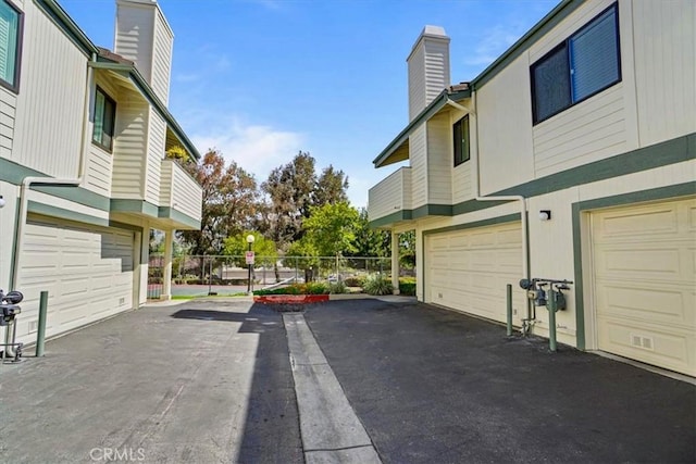 view of property exterior with an attached garage, fence, driveway, and a chimney