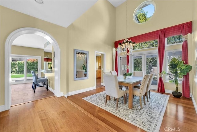 dining area with wood finished floors, arched walkways, baseboards, a high ceiling, and french doors