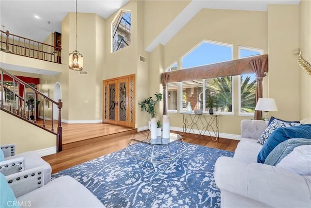 living room featuring a high ceiling, stairs, visible vents, and wood finished floors