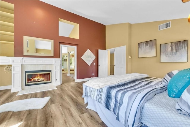 bedroom featuring visible vents, ensuite bathroom, baseboards, wood finished floors, and high vaulted ceiling
