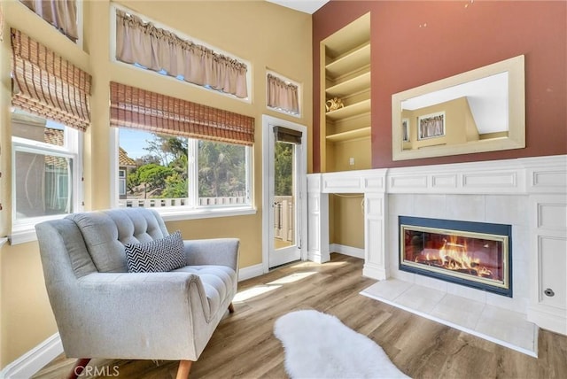 living area featuring a towering ceiling, a tiled fireplace, wood finished floors, and baseboards