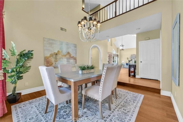 dining room featuring visible vents, a chandelier, baseboards, a towering ceiling, and wood finished floors
