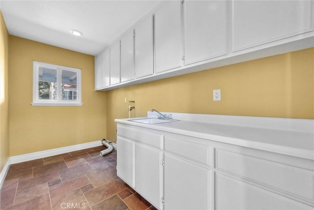 laundry room featuring stone finish floor, a sink, baseboards, hookup for a washing machine, and cabinet space