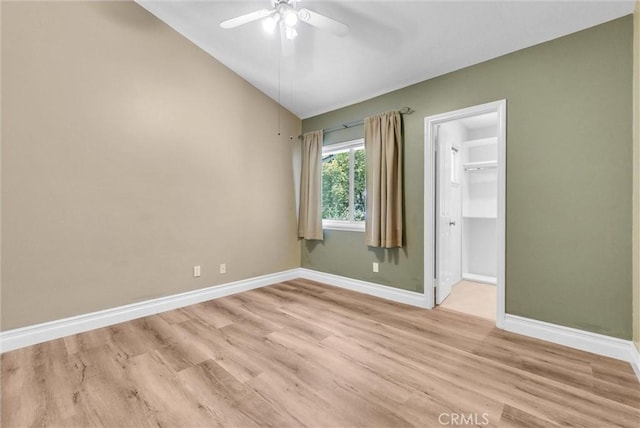 unfurnished bedroom with a walk in closet, baseboards, lofted ceiling, and light wood-type flooring