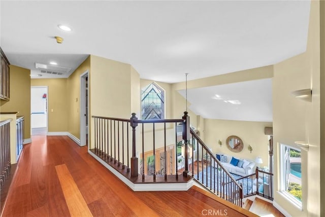 hall featuring baseboards, visible vents, wood finished floors, and an upstairs landing