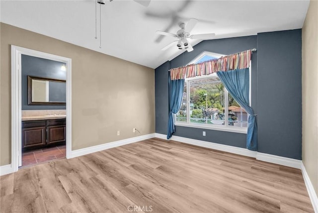 empty room featuring a ceiling fan, baseboards, vaulted ceiling, and light wood-style floors