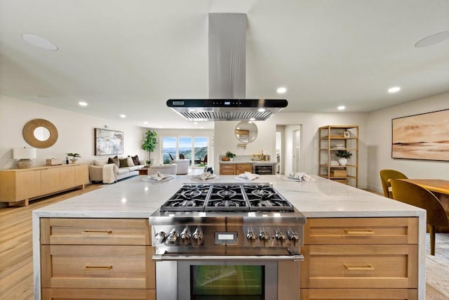 kitchen with recessed lighting, high end stainless steel range, light stone counters, island range hood, and open floor plan