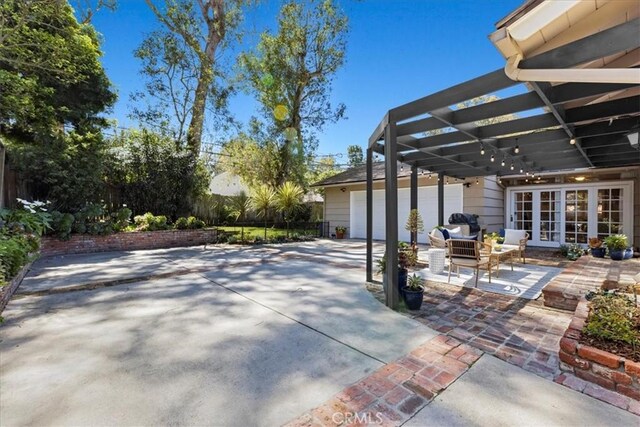 view of patio with an attached garage, french doors, concrete driveway, and a pergola