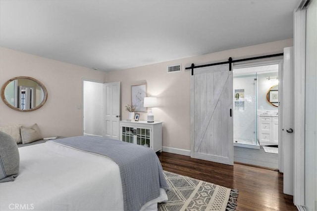 bedroom featuring visible vents, baseboards, wood finished floors, a barn door, and ensuite bath