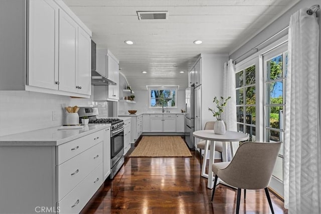 kitchen featuring light countertops, appliances with stainless steel finishes, dark wood-style floors, wall chimney range hood, and visible vents