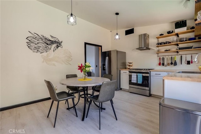 kitchen featuring light wood finished floors, light countertops, wall chimney range hood, a sink, and appliances with stainless steel finishes