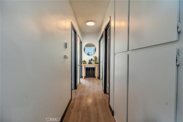 hall featuring light wood finished floors, baseboards, a textured ceiling, and visible vents