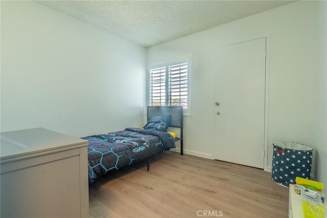 bedroom with baseboards, light wood-style floors, and a textured ceiling