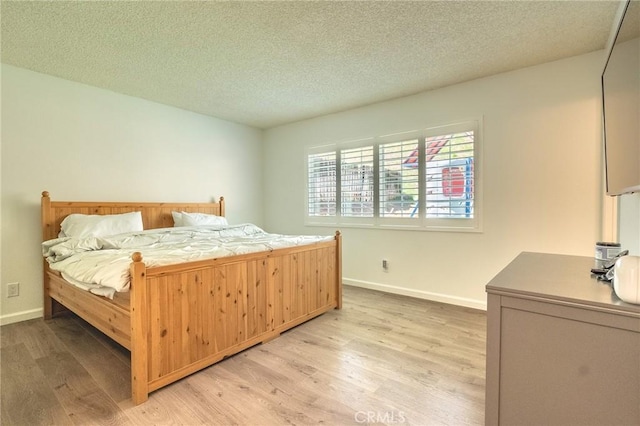 bedroom featuring light wood-style flooring, baseboards, and a textured ceiling