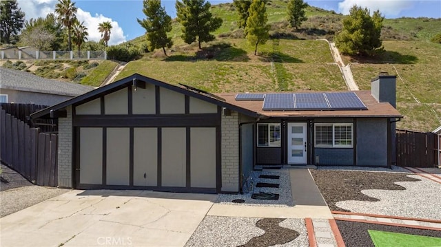 ranch-style home featuring fence, solar panels, an attached garage, driveway, and brick siding