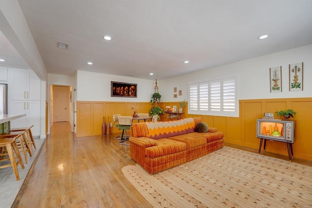 living area featuring visible vents, wainscoting, a decorative wall, and recessed lighting