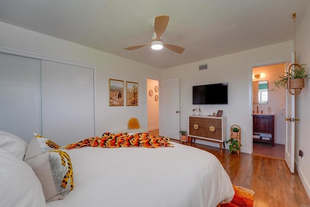 bedroom featuring a closet, ceiling fan, visible vents, wood finished floors, and ensuite bathroom