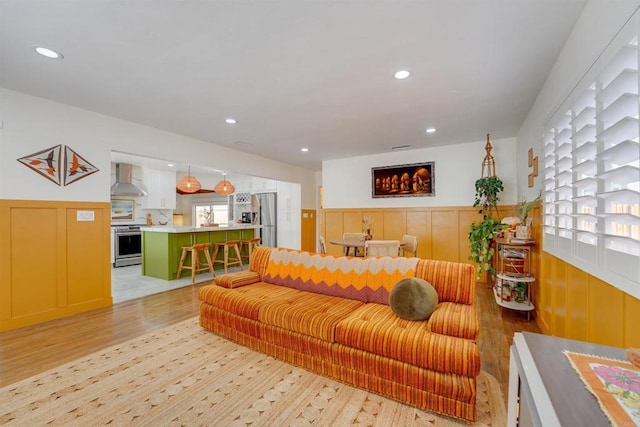 living area featuring recessed lighting, a wainscoted wall, light wood-style flooring, and a decorative wall