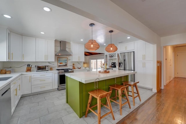 kitchen featuring white cabinets, stainless steel appliances, wall chimney exhaust hood, and a kitchen island