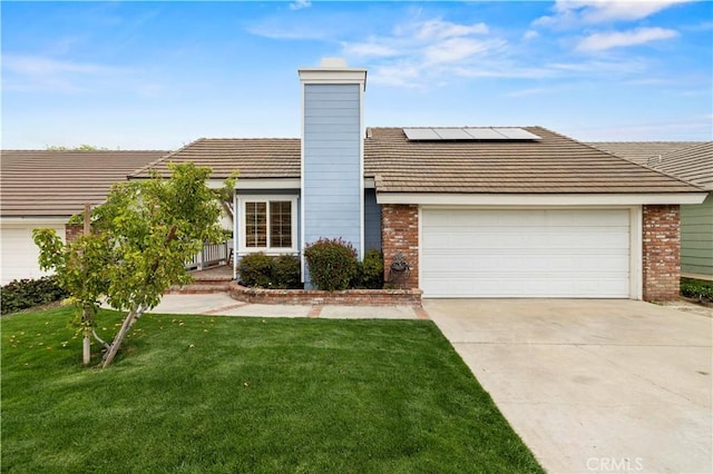 view of front of house with brick siding, solar panels, driveway, a front yard, and an attached garage